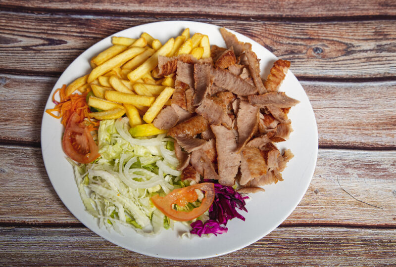 Beef doner on a plate with french fries and salad on wooden background. Beef doner on a plate with french fries and salad on wooden background.